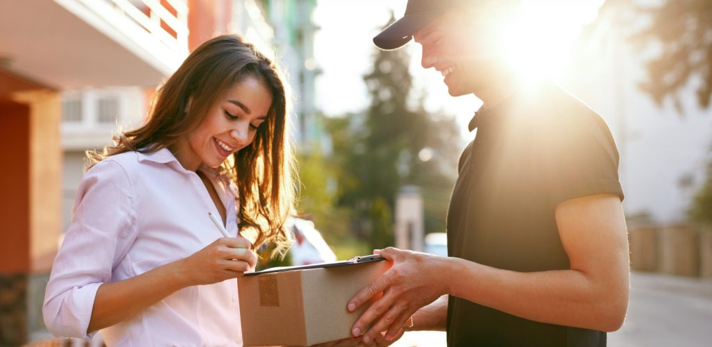 Courier Delivering Package To Woman. Client Signing Delivery Document, Receiving Box Near Home Outdoors. High Resolution